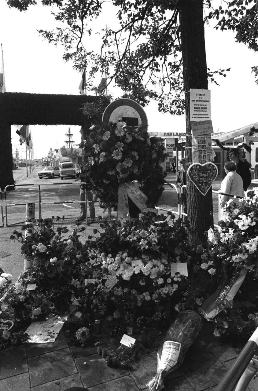 


                 Mehrere Blumen, Blumenkräne und Karten vor dem Haupteingang des Oktoberfests.
